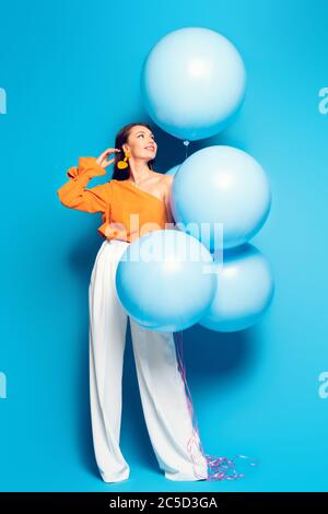 vue sur toute la longueur d'une femme à la mode avec de grands ballons festifs sur fond bleu Banque D'Images