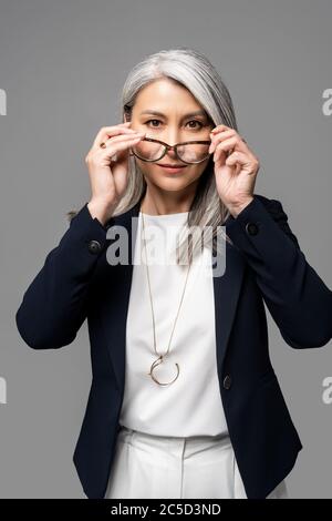 femme d'affaires asiatique sérieuse avec cheveux gris portant des lunettes isolées sur gris Banque D'Images