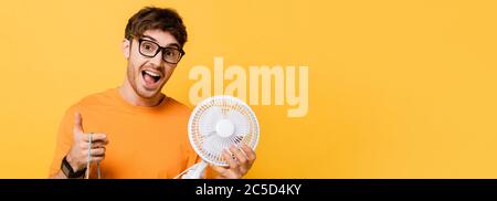 homme excité dans des lunettes tenant sac d'achats avec nouveau ventilateur électrique sur jaune, en-tête de site web Banque D'Images