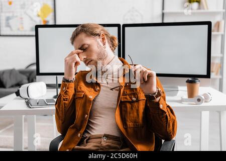 Artiste 3D fatigué tenant des lunettes près des appareils numériques sur une table au bureau Banque D'Images