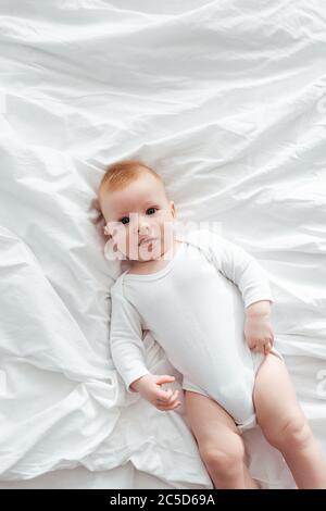 vue de dessus d'adorable petit garçon dans la barboteuse couché sur la literie et regardant l'appareil photo Banque D'Images