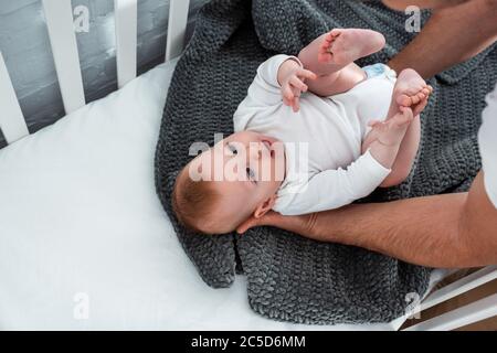 vue courte d'un homme touchant un joli petit garçon allongé dans un lit bébé sur une couverture Banque D'Images