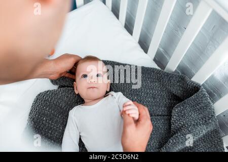 vue courte d'un homme touchant un adorable petit fils allongé dans un lit bébé sur une couverture, foyer sélectif Banque D'Images