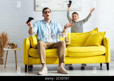 KIEV, UKRAINE - 9 JUIN 2020: Happy boy montrant le geste du gagnant près découragé père jouant au jeu vidéo Banque D'Images