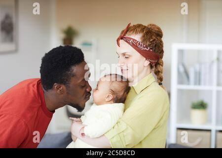 Jeune femme tenant bébé sur ses mains tandis que l'homme africain l'embrassant ils sont à la maison Banque D'Images