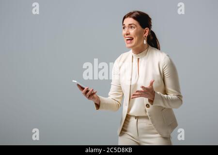 Femme d'affaires en colère tenant smartphone isolé sur gris, concept de corps positif Banque D'Images