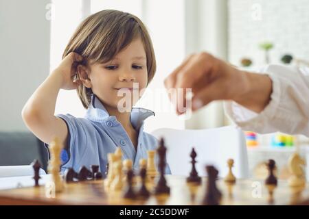 Adorable petit garçon jouant aux échecs avec sa mère à la maison. Enfant mignon appréciant jeu de stratégie de plateau avec ses parents à l'intérieur Banque D'Images