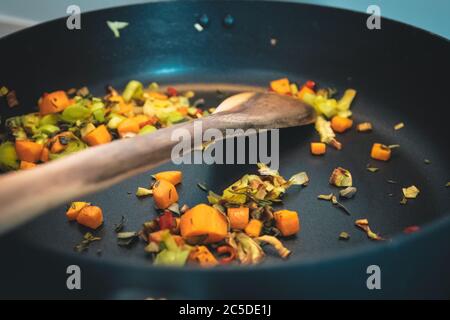 Gros plan de légumes sains cuits dans une casserole noire et une cuillère en bois Banque D'Images