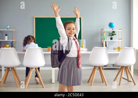 Concept de retour à l'école. Une écolière souriante lui a permis de lever les mains tout en étant debout en classe. Banque D'Images