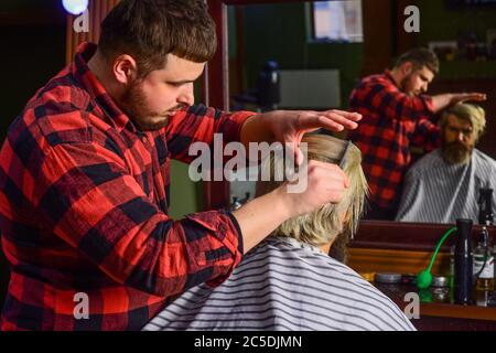 Client Hipster se couper la coiffure. Coiffeur professionnel dans l'intérieur de la barbershop. Coiffeur et client. Coiffure travaille coiffure pour homme barbu arrière-plan de barbershop. Gars avec de longs cheveux teints blond. Banque D'Images