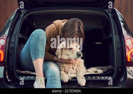 Une jeune femme se fait huer en or en étant assise dans le coffre ouvert de voiture noire Banque D'Images
