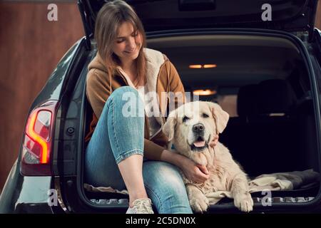 Jeune femme en jeans bleu à côté de l'Golden retriever assis dans le coffre ouvert d'une voiture noire Banque D'Images