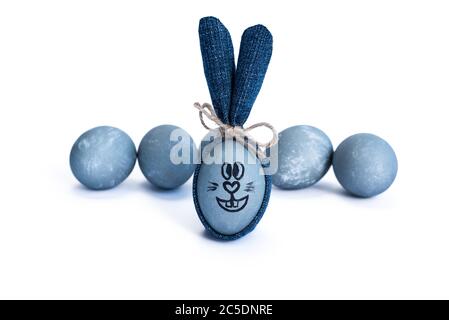 Mignon lapin de Pâques avec oreilles en denim bleu et rangée d'œufs en couleur de béton sur fond blanc. Idée de bricolage. Copier l'espace. Carte de vœux de Pâques Banque D'Images
