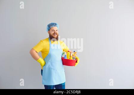 Drôle de gros gars avec des fournitures de nettoyage sur fond gris, l'espace de copie. Travailleur sanitaire qui fait des tâches domestiques Banque D'Images