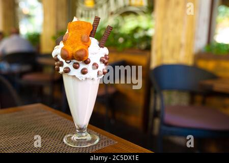 Laissez refroidir le milkshake avec des biscuits et des boules de chocolat. Milk-Shake dans un bécher en verre sur une table sur une plate-forme de rue dans un café. Boissons rafraîchissantes en été. Banque D'Images