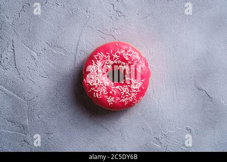 Donut rose avec saupoudrés, dessert glacé sucré sur fond texturé en béton, vue du dessus Banque D'Images