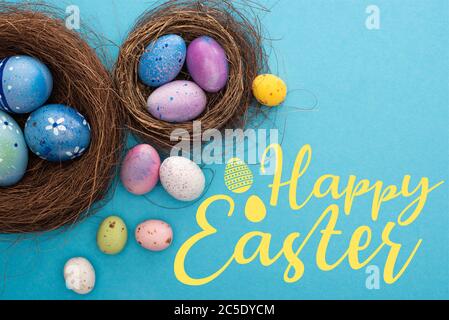 Vue de dessus des oeufs de Pâques colorés dans les nids sur fond bleu avec illustration joyeuses Pâques Banque D'Images