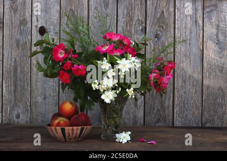 Un vase de fleurs d'été à côté d'un bol en céramique fait main rempli de pêches Banque D'Images