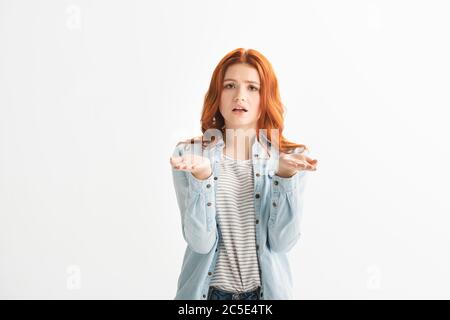 confusion de la tête rouge de l'adolescence fille dans des vêtements en denim avec le geste hauturé, isolé sur blanc Banque D'Images