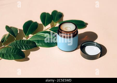 Pot de crème à l'huile essentielle avec des feuilles de plantes naturelles sur fond beige. Banque D'Images