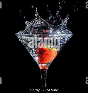 Fraisier éclaboussant dans un verre de martini sur fond noir Banque D'Images
