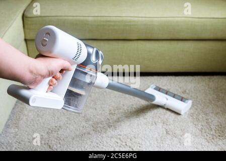 Aspirateur sans fil utilisé sur la moquette dans la chambre. Pour les travaux ménagers avec un nouveau aspirateur droit. Personne peut accueillir un aspirateur blanc moderne près d'un canapé. Nettoyage à la maison, env Banque D'Images