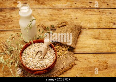 Lait d'avoine végétalien, lait de substitution non laitier. Sécher les flocons dans un bol en céramique, un flacon en verre, de l'avoine. Arrière-plan en bois vintage, espace de copie Banque D'Images