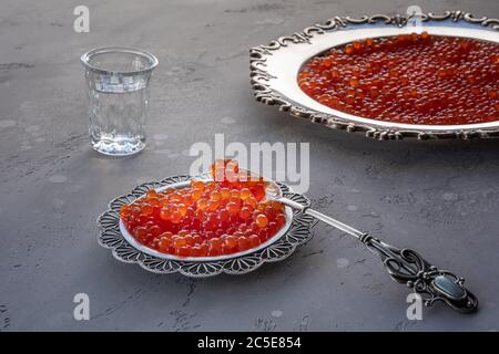 Caviar rouge en cuillère argentée et assiette sur fond gris. Vodka et un plat de caviar sur fond non focalisé. Mise au point sélective. Conce saine alimentation Banque D'Images