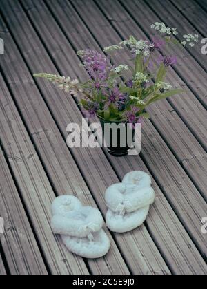 Fleurs sauvages dans un vase et chaussons doux sur un plancher en bois. Banque D'Images