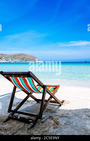 Une chaise longue se tient à l'ombre sur les rives d'une plage de sable au bord de la mer. La couleur de l'eau et le ciel bleu avec des nuages cassés dans le b Banque D'Images