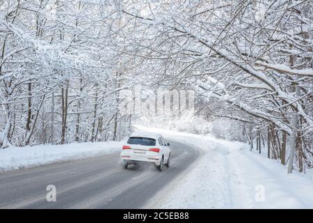 Route en forêt d'hiver. Une voiture blanche traverse les bois après la chute de neige. Vue panoramique sur le tunnel avec des arbres enneigés. Beau paysage de neige gelée couverte. Banque D'Images
