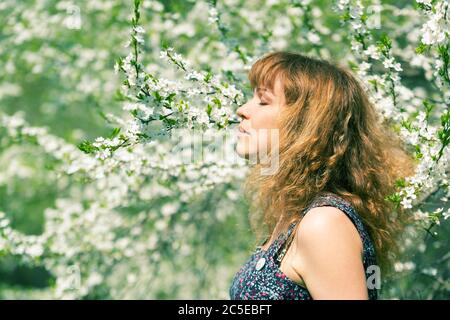 Jeune femme aux yeux fermés qui sent les cerisiers en fleurs Banque D'Images