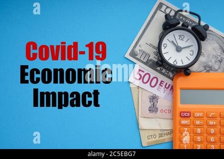 COVID19 texte D'IMPACT ÉCONOMIQUE avec réveil, billets de banque et calculatrice sur fond bleu. Coronavirus Covid19 et Business concept Banque D'Images