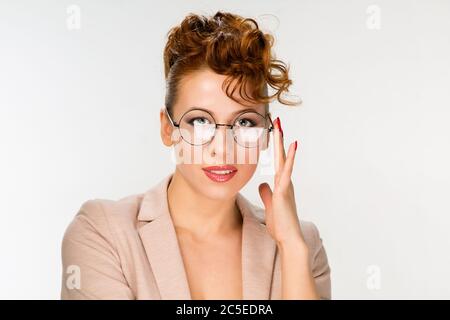 Gros plan de jeune femme attrayante isolée sur fond gris, portant de grands lunettes rondes avec un cadre noir fin, touchant des taches avec les doigts, smili Banque D'Images