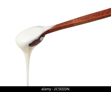 vue latérale du miel blanc naturel biologique versé à partir d'une petite cuillère en bois, isolée sur fond blanc Banque D'Images