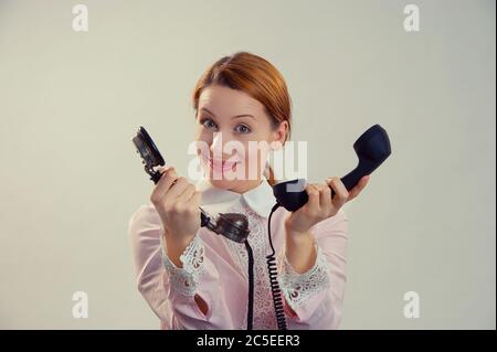 Appelle-moi. Une femme excitée et confuse se se tenant, donnant deux téléphones et regardant sourire à la caméra. Caucasien Business personne, chemise rose formelle, tête rouge gi Banque D'Images