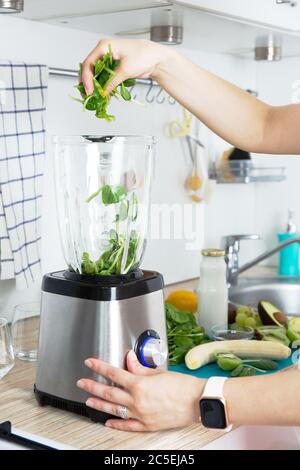 Les mains des filles préparent un smoothie vert, met des feuilles d'épinards frais dans un mélangeur. Concept de saine alimentation. Végétarisme, nourriture végétalienne, nourriture de forme physique, détox Banque D'Images