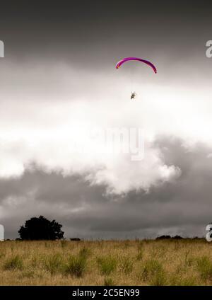 Parapente rose volant haut dans un ciel orageux Banque D'Images