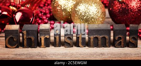 Le mot NOËL écrit avec des blocs d'imprimante en bois vintage. Message de Noël sur bois ancien avec décorations traditionnelles d'arbre derrière. Banque D'Images