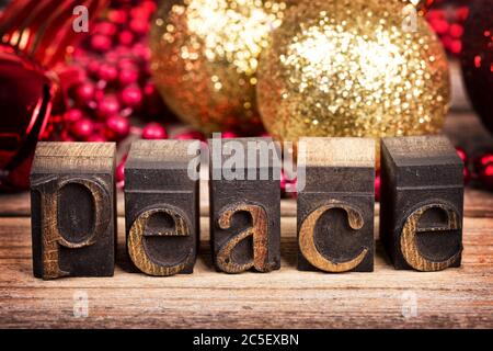 Le mot PAIX écrit avec des blocs d'imprimante en bois vintage. Message de Noël sur bois ancien avec décorations traditionnelles d'arbre derrière. Banque D'Images
