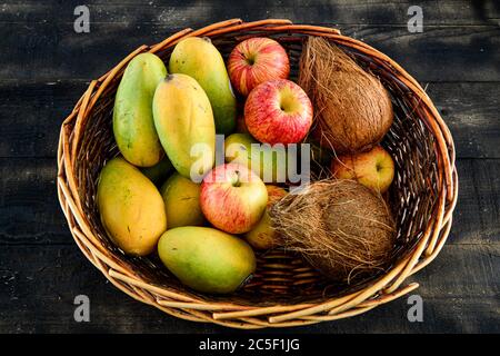 dans un panier sur fond de bois noir, mélanger les fruits, la mangue, la noix de coco et la pomme Banque D'Images