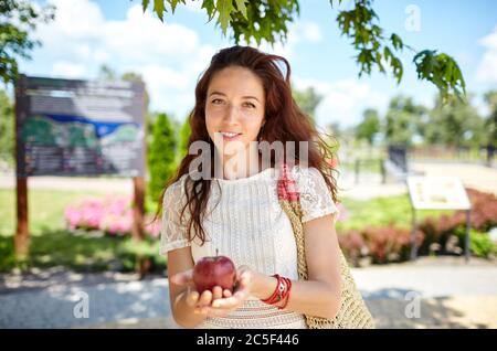 Belle femme attrayante tenant la pomme dans le parc d'été.caucasienne fille apprécie un style de vie d'été lumineux. Banque D'Images