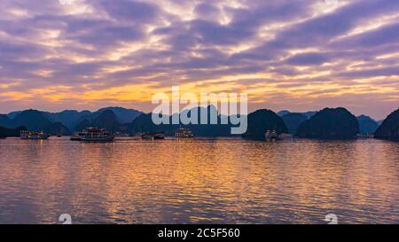 Des bateaux de tourisme illuminés au coucher du soleil sur la baie de Halong, au Vietnam Banque D'Images