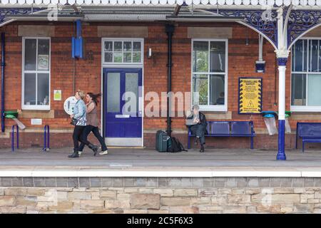 Les passagers de la gare de Stalybridge se précipitent le long de la plate-forme et sur un banc au téléphone Banque D'Images