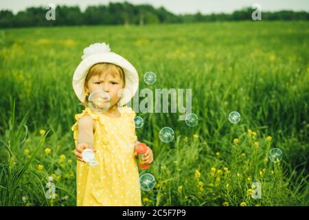 Jeune fille dans une robe jaune marchant sur le terrain et et des bulles de soufflage. Heure d'été. Banque D'Images