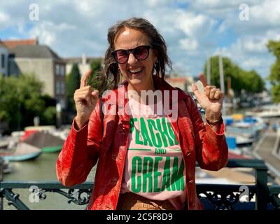 Portrait d'une femme mature et plus jeune, portant des lunettes de soleil et une veste en cuir rouge vintage, adossée à une main courante, montrant l'émotion souriante. Banque D'Images