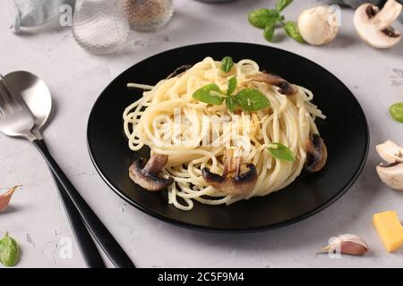 Spaghetti aux champignons et basilic sur plaque noire sur fond gris, gros plan, format horizontal Banque D'Images