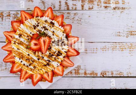 Crème fouettée avec sauce fraise et caramel sur fond blanc en bois. Banque D'Images