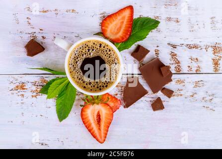 Café naturel foncé avec fraise et chocolat sur table en bois blanc. Vue de dessus. Banque D'Images