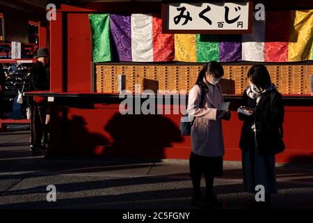 Deux amis lisant le 'o-mikuji' (prophéties aléatoires écrites sur des bandes de papier) au temple Senso-ji. Tokyo, Japon. Banque D'Images